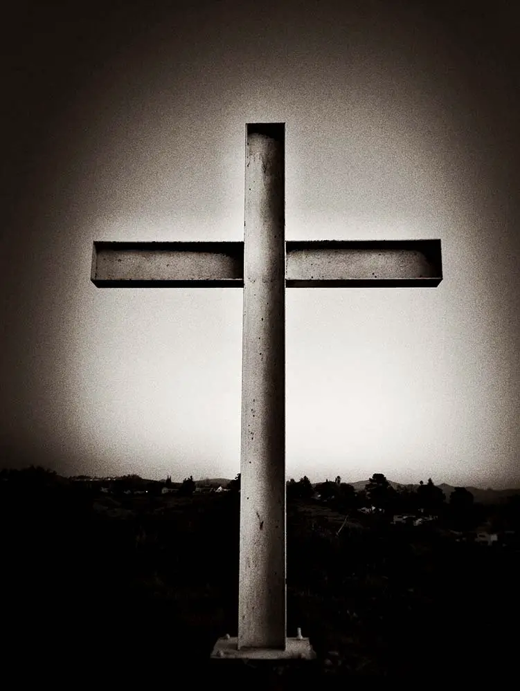 Metal cross on hillside, black and white.