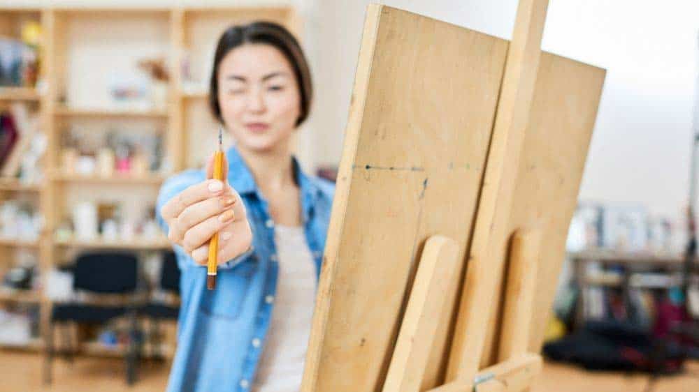 An artists measuring by holding up her thumb and pencil.