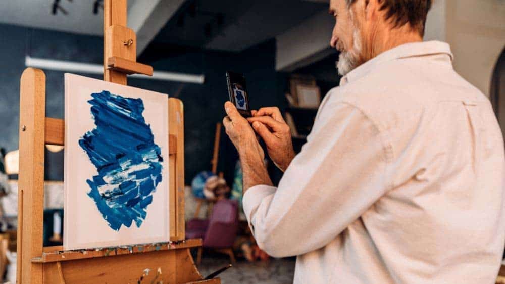 An artist using a mobile phone to take pictures of his artwork.